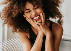 A cheerful woman with an afro hairstyle sitting indoors, showcasing happiness and style.